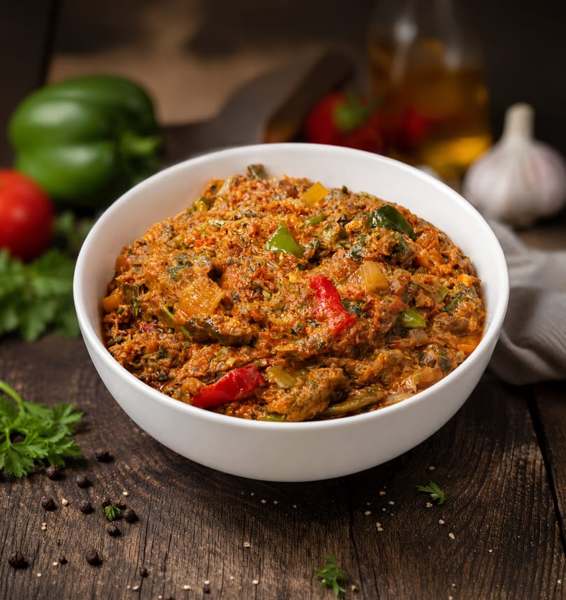 A white bowl filled with a rich, savory stew featuring vegetables and spices on a wooden table.