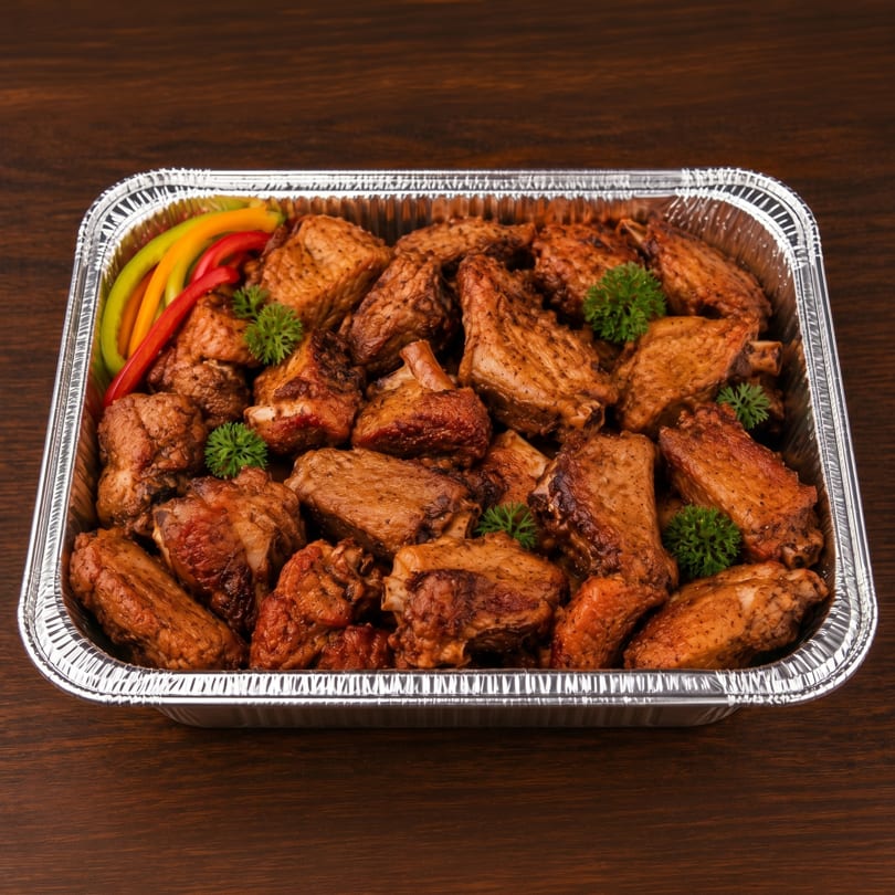 A foil tray filled with seasoned chicken wings and drumettes, garnished with bell pepper strips and parsley.
