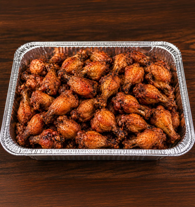A large foil pan filled with dozens of crispy, seasoned chicken drumettes and wingettes.