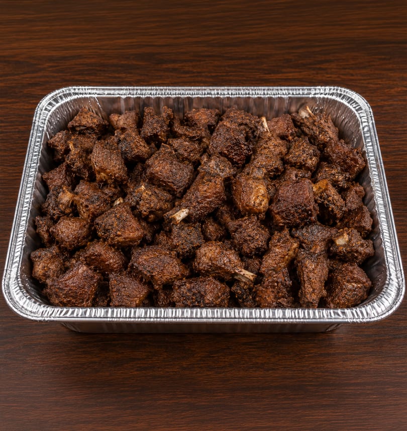 A large aluminum catering pan filled with numerous pieces of dark, crispy fried chicken on a wooden table.