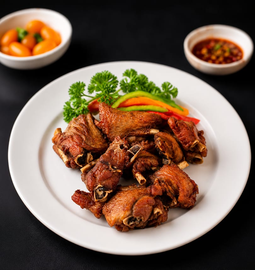 Crispy fried duck pieces on a white plate with parsley, bell peppers, and dipping sauces.